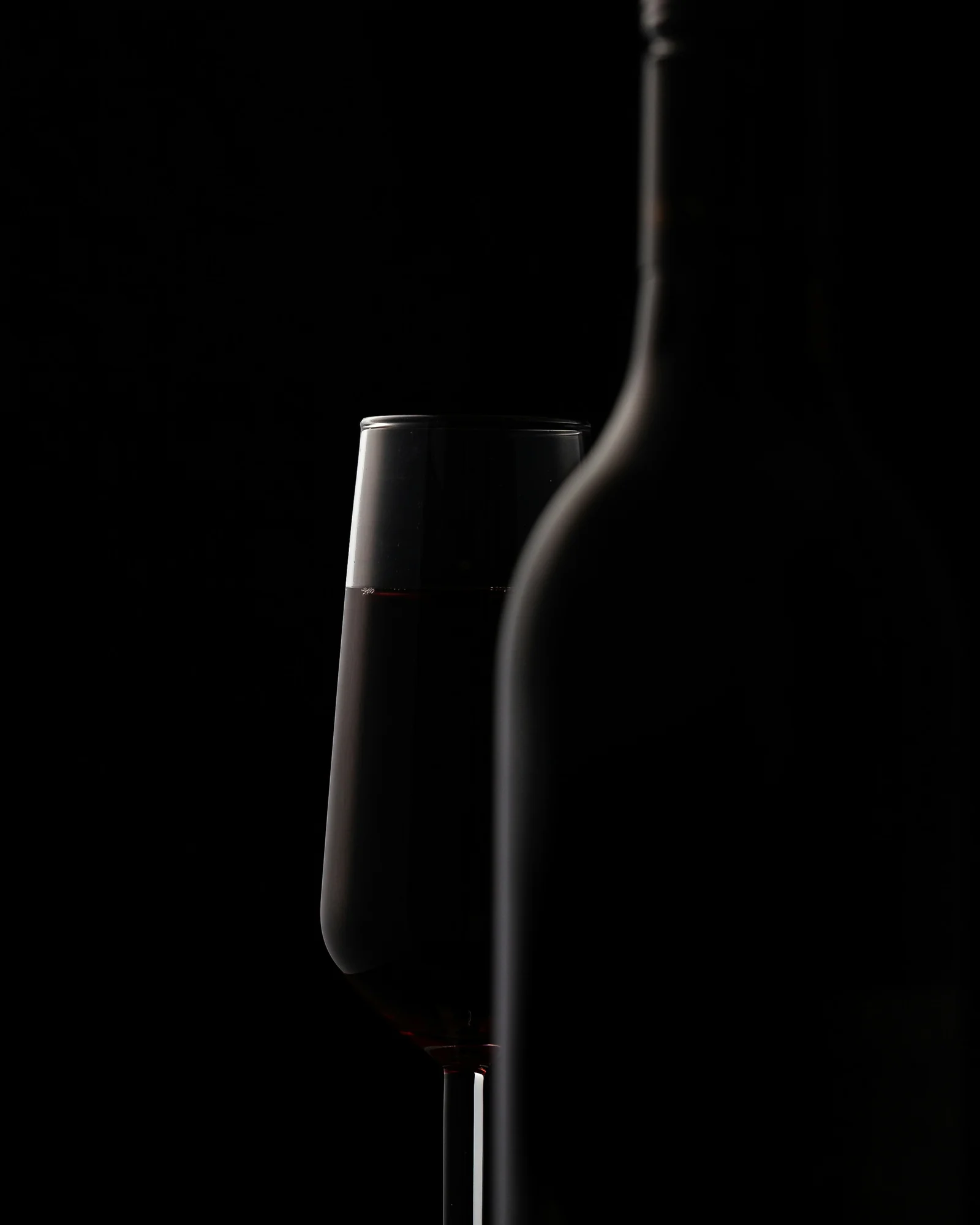 A wine glass and bottle silhouette against a nearly black background.